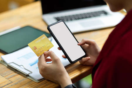 Cropped shot female holding phone and credit card, office desk in the background, online...