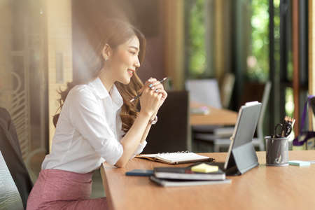 Young female manager feeling happy with her work, online meeting, online work interview with digital tablet and office supplies on wood tableの写真素材