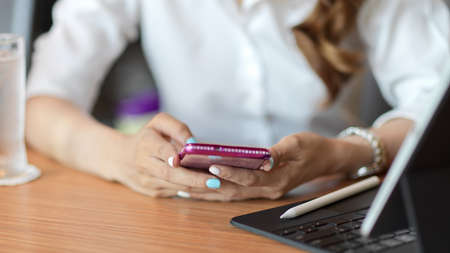 Close up hand, female using smartphone on table with tablet and stylus pen on woody table, checking news, social networkの写真素材