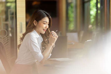 Businesswoman sitting indoor at office, thinking about work happily and positivelyの写真素材