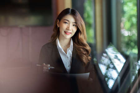 Charming businesswoman portrait, female assistant holding papers and pen at officeの写真素材