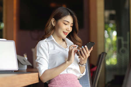 Beautiful girl looking at mobile phone, businesswoman texting to her friends while lunch break at officeの写真素材