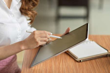Close up, businesswoman sitting and using wireless tablet pc with blur blank empty screen at office desk, cropped shotの写真素材