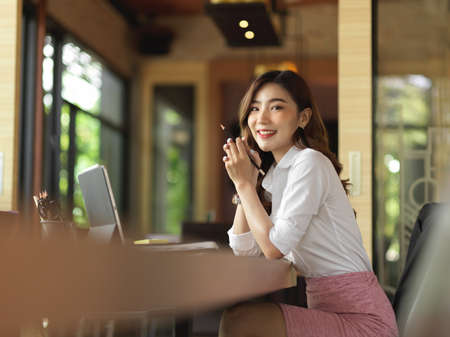 Beautiful millennial businesswoman sitting and daydreaming her work promotion at her office desk, attractive female secretaryの写真素材