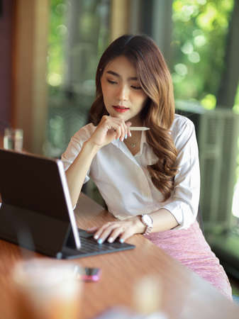 Portrait of serious successful working woman thinking about her work with digital tablet, holding stylus pen at officeの写真素材