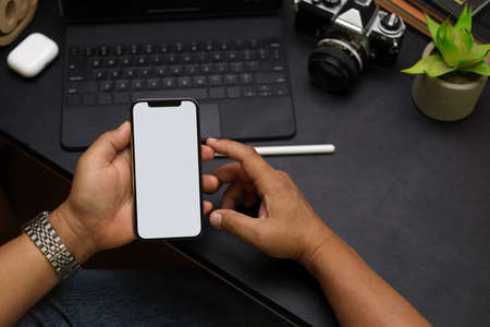 Close up male hands, using smartphone to work online from home office, phone blank screen mockup, portable tablet, camera, decor on black workspace, black backgroundの写真素材