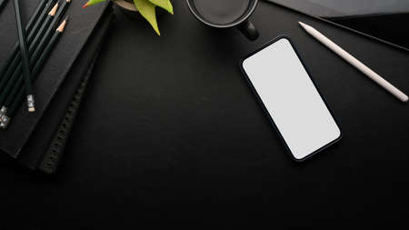 Modern smartphone white screen mockup on black empty space with gadget, coffee, notebooks, pencils, black background, overheadの写真素材
