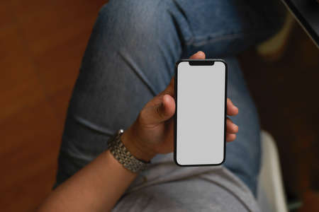 Male in casual looks sitting and holding smartphone mockup, relaxing in his breaking times, reading e-newsの写真素材