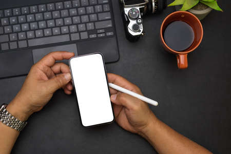 Close up, overhead male hands, reading news on the internet via smartphone, smartphone white screen mockup, coffee in the morning, tablet, camera, black workspaceの写真素材