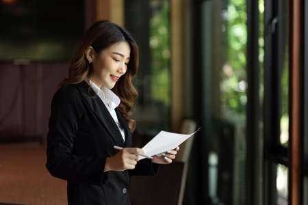 Peaceful businesswoman standing and reading business contract against of the glass wall at officeの写真素材