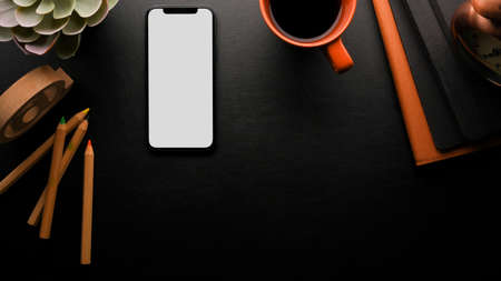 Workspace in black background with copy space, smartphone white screen mockup, black coffee, colour pencils, accessories,の写真素材