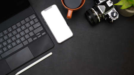 Freelance photographer working desk concept with smartphone mockup, portable tablet, camera, black coffee, house plant and copy space on black background, top viewの写真素材