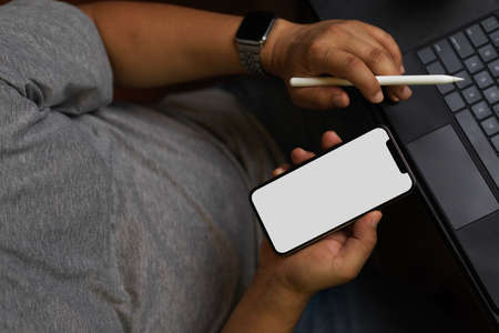 Success man in casual sitting and using smartphone to work, phone blank screen mockup, tablet, holding stylus pen, black workspaceの写真素材