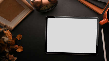 Modern workspace with tablet white screen mockup, blank wood frame template mockup, dry flower, vintage alarm clock, notebooks, coffee on black background, black desk, flat layの写真素材