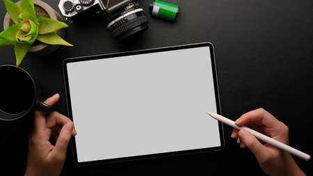 Close up hands top view, female hands holding stylus pen to sketching design, designer workspace concept, tablet mockup, camera, coffee, plant on black backgroundの写真素材