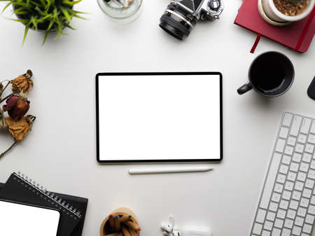 Digital smart tablet blank screen mockup surrounded by accessories stuff, keyboard, camera, books, dry flower, plants coffee on white backgroundの写真素材