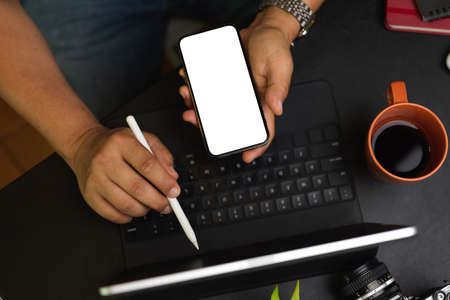 Male freelancer using smartphone and tablet to analysing business data at co-working space, device in blank screen, modern black workspaceの写真素材