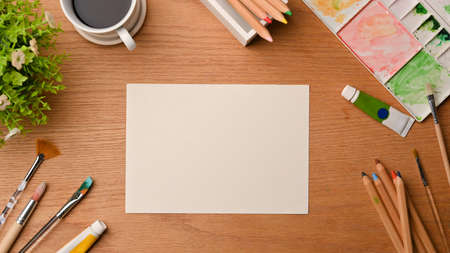 Creative art workspace, blank paper sheet for your project surrounded by painting tools, water colour, palate, stationery on wooden background, top viewの写真素材