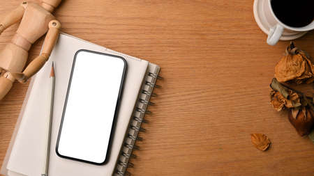 Flat lay, top view, cozy and warm workspace, wooden background with smartphone mockup, wood figure, notebook, dry flowers, black coffee, copy space,の写真素材
