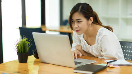 Focused beautiful asian woman using laptop, look at laptop screen, reading working emailの写真素材