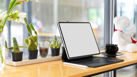 Smart tablet blank screen mockup on wooden desk with cactus, coffee cup and blurred window glass in the backgroundの写真素材