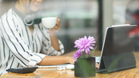 Happy millennial freelancer working, checking email on tablet and drinking morning tea for brunch at coffee shop, cropped shotの写真素材
