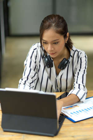 Smiling attractive young hipster woman working on tablet, headphone for listen music, chilling worker using tablet, portraitの写真素材