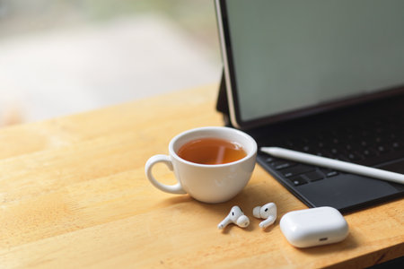 A cup of tea with tablet screen mockup, earbuds, stylus pen, copy space on wooden table, close up, cropped shotの写真素材