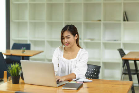 Elegant female college student sitting and using laptop computer in library co-working spaceの写真素材