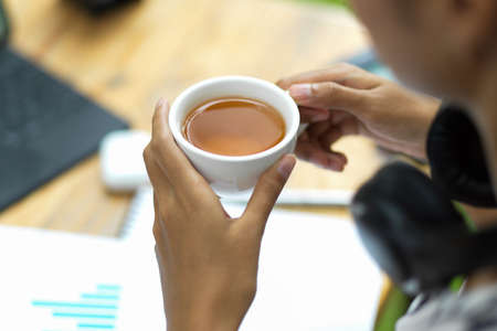 Business female worker drink hot tea during work with business papers at office, close up, cropped shotの写真素材
