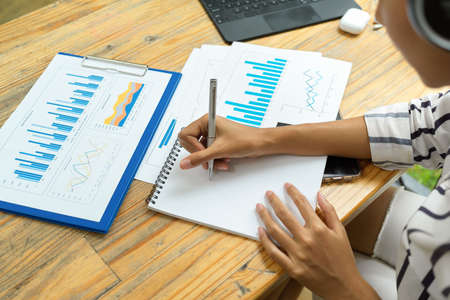 Close up, female financial worker taking notes about business finance to analyse at office, financial papers, financial bar graphの写真素材
