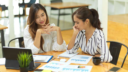 Female co-worker brainstorming looking on tablet and financial data report at office desk, communication conceptの写真素材