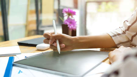 Close up, female hand using stylus pen for drawing on graphic portable tablet at cozy work placeの写真素材
