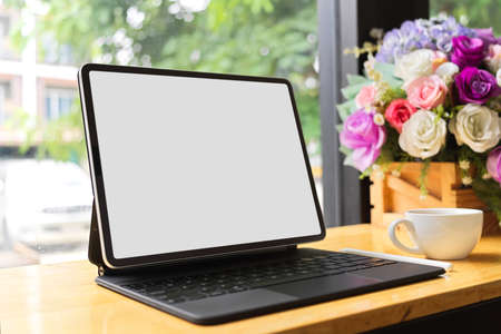 Tablet blank screen mockup with keyboard stand in wooden table at coffee shop, blurred window view in the backgroundの写真素材