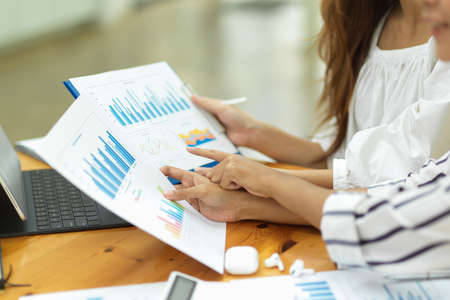 Closeup, cropped shot, two businesswoman analysing business finance together, looking at financial bar graph in officeの写真素材