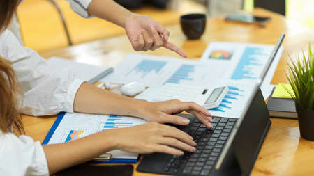 Close up, cropped shot, focus hands, two businesswoman working together, digital tablet, paperworks on wooden tableの写真素材