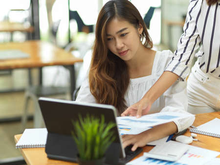 Success businesswoman teaching and guiding her assistant at workplace, laptop, business papersの写真素材