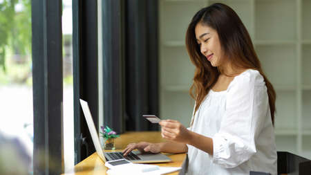 Side view, Young woman holding credit card using laptop to pay on online shoppingの写真素材