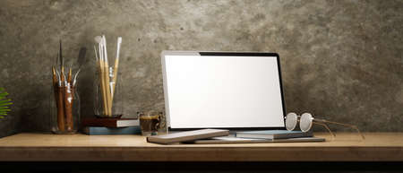 Hipster artist working space with laptop blank screen mockup, books, glasses, painting brushes, painting tools on wood desk, rusty loft wall interior, 3d rendering, 3d illustrationの写真素材