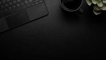 Modern dark leather desk with mockup place, keyboard, a cup of black coffee, plant, black background, overhead, top viewの写真素材