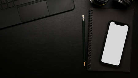 Closeup, top view, modern dark study table, minimal style, smartphone screen mockup on black notebooks, pencil, laptop, on black surfaceの写真素材