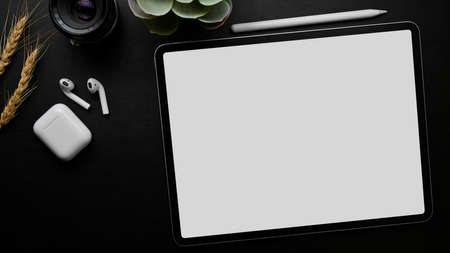 Dark minimal working table, graphic tablet empty screen mockup, stylus, earbuds, camera lens on black background, top view, close upの写真素材