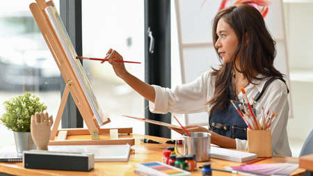 Talented female artist painting with water colour on canvas in art studio, easel, painting toolsの写真素材