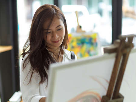 Closeup of beautiful female artist smiling while painting on canvas easel, relaxation hobby, inspiration painterの写真素材