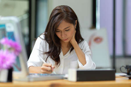 Attractive female using stylus and digital tablet, hand on chin, thinking about work, concentratedの写真素材