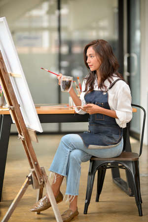 Portrait of beautiful art student sitting, holding coffee, art palette, paint brush, get an inspired, young talented artist workingの写真素材