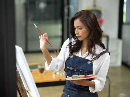 Talented female artist having inspired facial expression, passion drawing, holding art palette and...