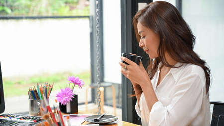 Female feeling clam, drink and smell hot tea while looking at art piece, painting tools on tableの写真素材