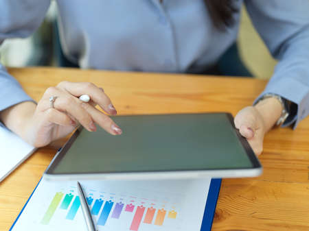 Closeup, businesswoman using tablet computer for create new report, reading client contract from tablet, financial graph report on tableの写真素材