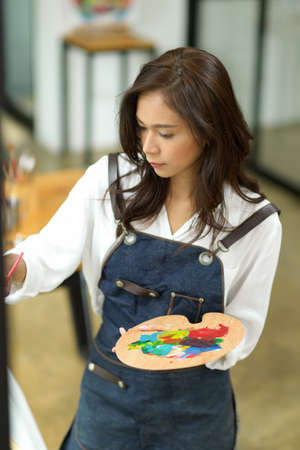 Portrait of female painter, painting art piece with oil colour on canvas at workshop